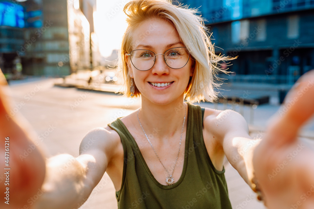 Young blonde woman tourist wearing glasses makes selfie on the background of modern glass buildings in the city center