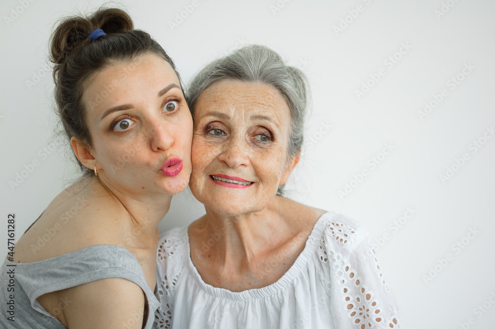Happy senior mother is hugging her adult daughter, the women are laughing together, sincere family of different age generations having fun on white background, mothers day. Happy senior mother is hugging her adult daughter, the women are laughing together, sincere family of different age generations having fun on white background, mothers day.