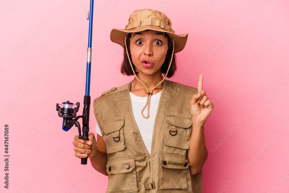 Young mixed race fisherwoman holding a rod isolated on pink background having some great idea, concept of creativity. Young mixed race fisherwoman holding a rod isolated on pink background having some great idea, concept of creativity.