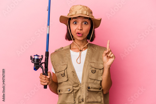 Young mixed race fisherwoman holding a rod isolated on pink background having some great idea, concept of creativity.