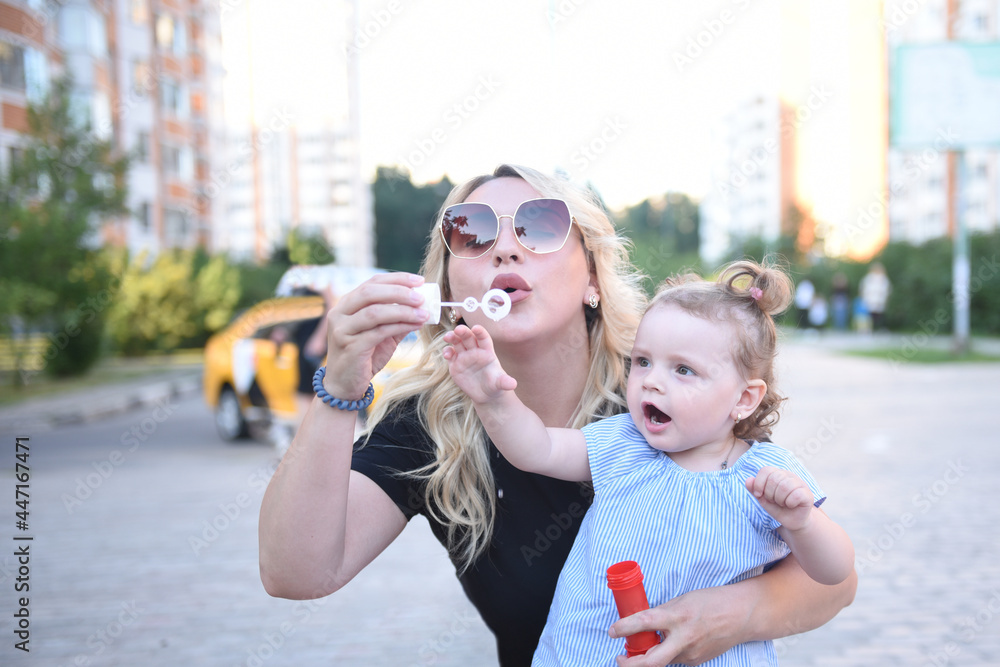 A young blonde mom in sunglasses teaches her little daughter to blow and blow soap bubbles A young blonde mom in sunglasses teaches her little daughter to blow and blow soap bubbles