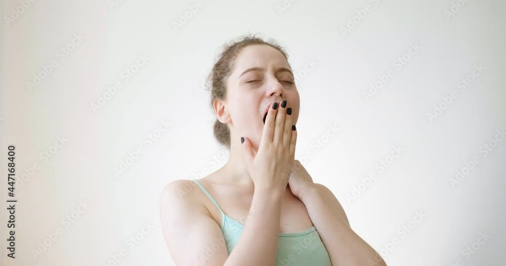 A young woman with a T-shirt yawns and rubs her neck. A young woman with a T-shirt yawns and rubs her neck.