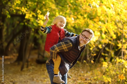 Fototapeta Little boy and his father having fun during stroll in the forest on sunny autumn day