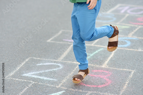 Little boy s legs and hopscotch drawn on asphalt. Child playing hopscotch game on playground on spring day.