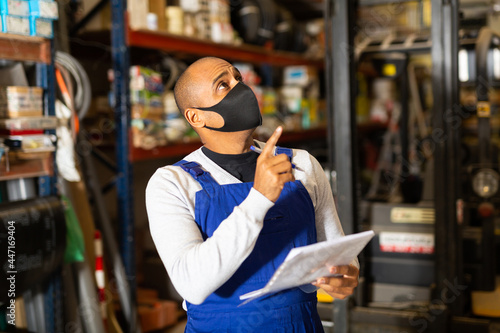 Warehouse manager in protective mask calculates the quantity of goods and writes it down in a notebook © JackF