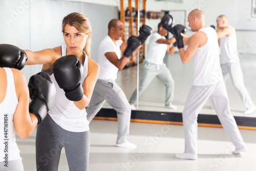 Concentrated woman practicing boxing punches in sparring during group self defence course in gym