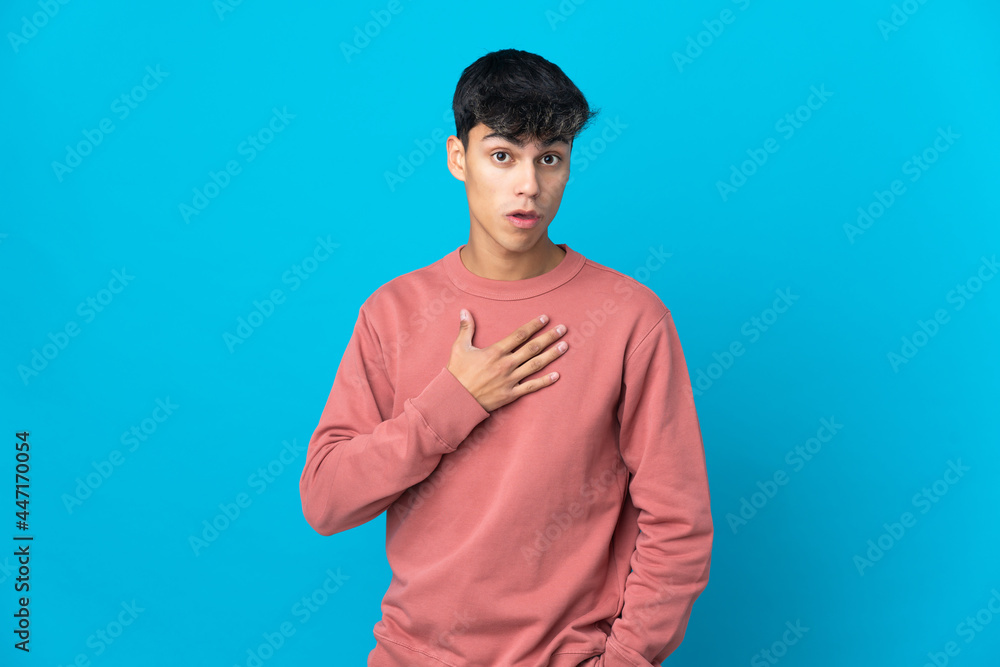 Young man over isolated blue background surprised and shocked while looking right Young man over isolated blue background surprised and shocked while looking right