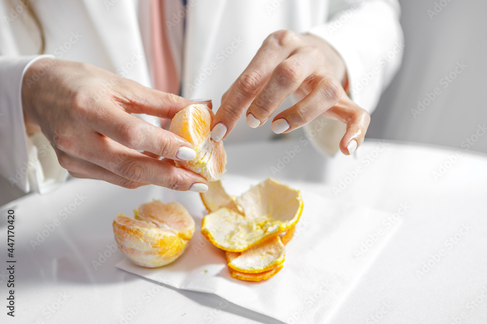 A woman is peeling a ripe orange. Hands close-up.