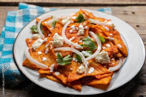 Mexican food. Red chilaquiles with cheese and sour cream on wooden background