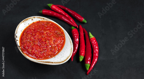 Paste harissa sauce in a bowl on a black background close up. Adjika hot chili peppers sauce. Copy space. photo