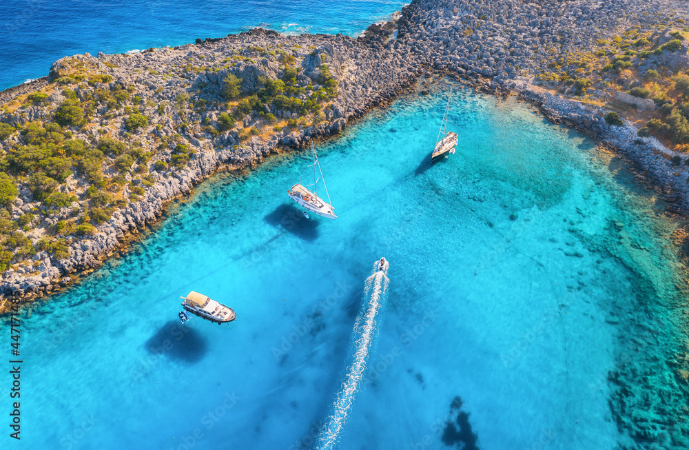 Aerial view of beautiful yachts and boats on the sea at sunset in summer. Akvaryum koyu in Turkey. Top view of luxury yachts, sailboats, clear blue water, rock, stone, mountain and green trees. Travel