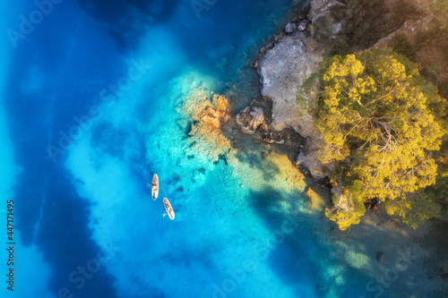 Aerial view of people on floating sup boards on blue sea, rocks, trees at sunset in summer. Blue lagoon, Oludeniz, Turkey. Tropical landscape. Kayaks on clear water. Active travel. Top view of canoe