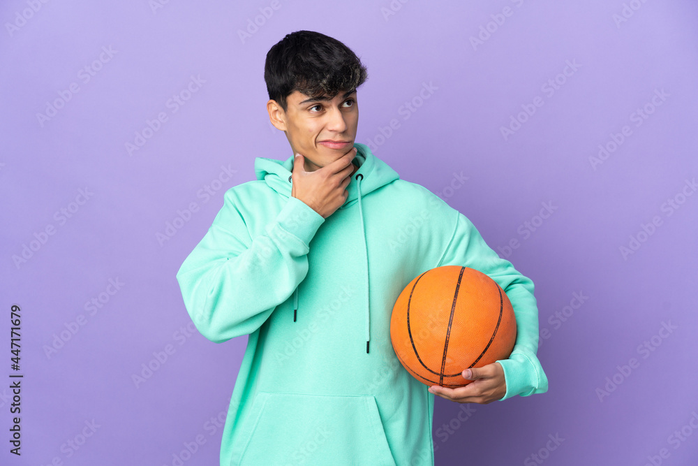 Young man playing basketball over isolated purple background having doubts