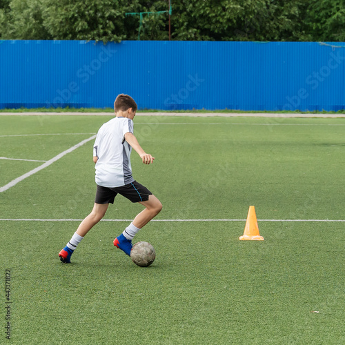 The boy loves to play football, trains with the ball on the artificial turf and scores a goal. The boy plays football © Viacheslav