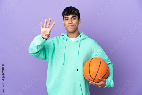 Young man playing basketball over isolated purple background happy and counting four with fingers © luismolinero
