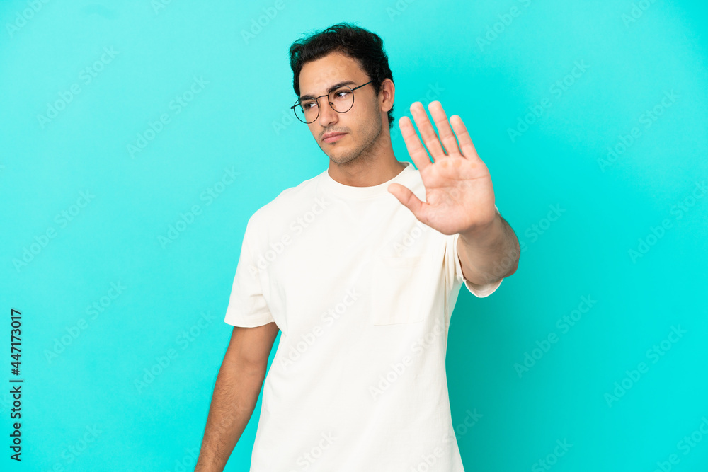 Caucasian handsome man over isolated blue background making stop gesture and disappointed Caucasian handsome man over isolated blue background making stop gesture and disappointed