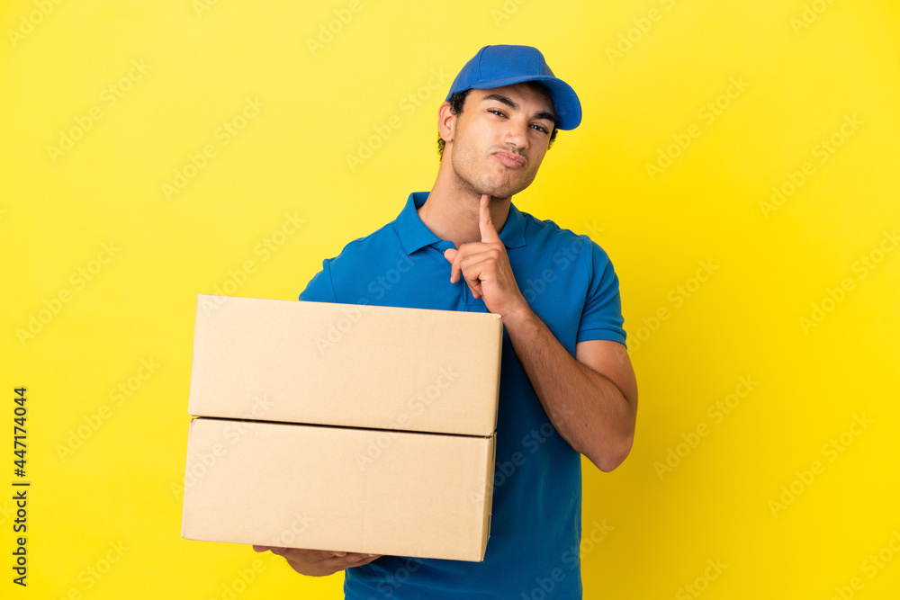 Delivery man over isolated yellow wall having doubts while looking up Delivery man over isolated yellow wall having doubts while looking up