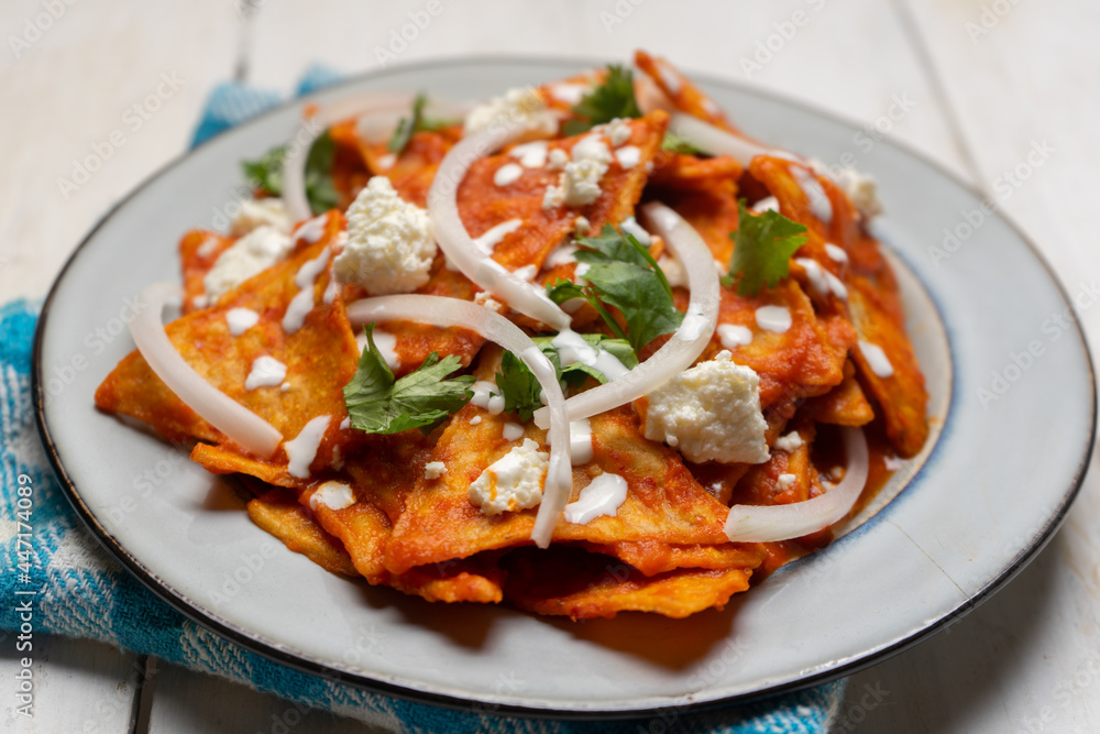 Mexican food. Red chilaquiles with cheese and sour cream on white background Mexican food. Red chilaquiles with cheese and sour cream on white background