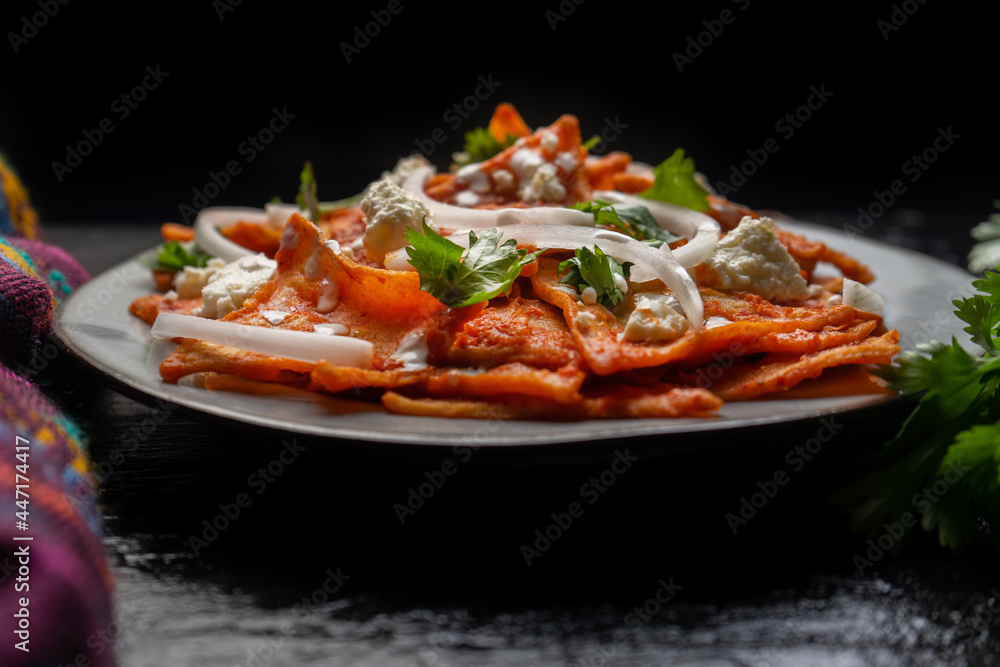 Mexican food. Red chilaquiles with cheese and sour cream on dark background Mexican food. Red chilaquiles with cheese and sour cream on dark background