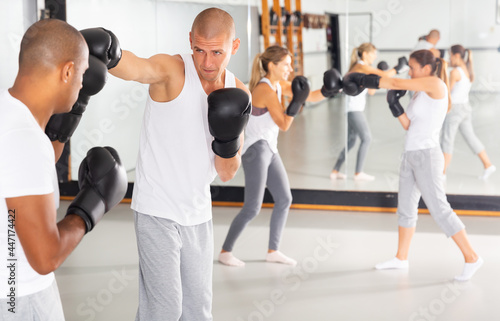 Emotional adult man mastering self defense techniques, practicing punches during sparring at boxing gym