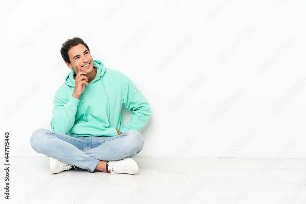Caucasian handsome man sitting on the floor thinking an idea while looking up Caucasian handsome man sitting on the floor thinking an idea while looking up