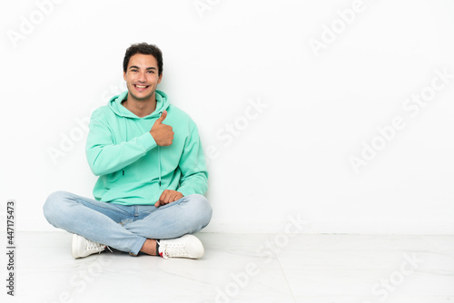 Caucasian handsome man sitting on the floor giving a thumbs up gesture