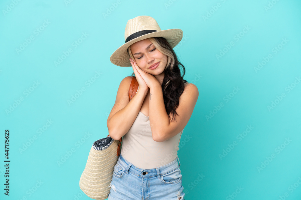 Teenager Russian girl with pamel and beach bag isolated on blue background making sleep gesture in dorable expression Teenager Russian girl with pamel and beach bag isolated on blue background making sleep gesture in dorable expression