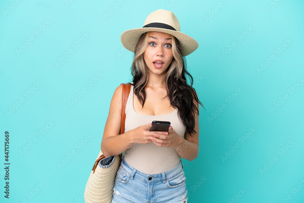 Teenager Russian girl with pamel and beach bag isolated on blue background surprised and sending a message Teenager Russian girl with pamel and beach bag isolated on blue background surprised and sending a message