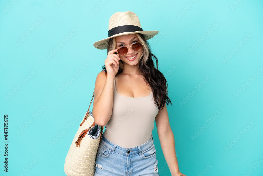Teenager Russian girl with pamel and beach bag isolated on blue background with glasses and happy Teenager Russian girl with pamel and beach bag isolated on blue background with glasses and happy