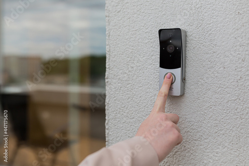 Slika na platnu woman's hand uses a doorbell on the wall of the house with a surveillance camera