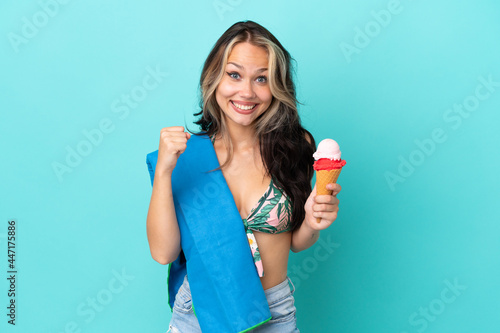 Teenager caucasian girl holding ice cream and towel isolated on blue background celebrating a victory in winner position