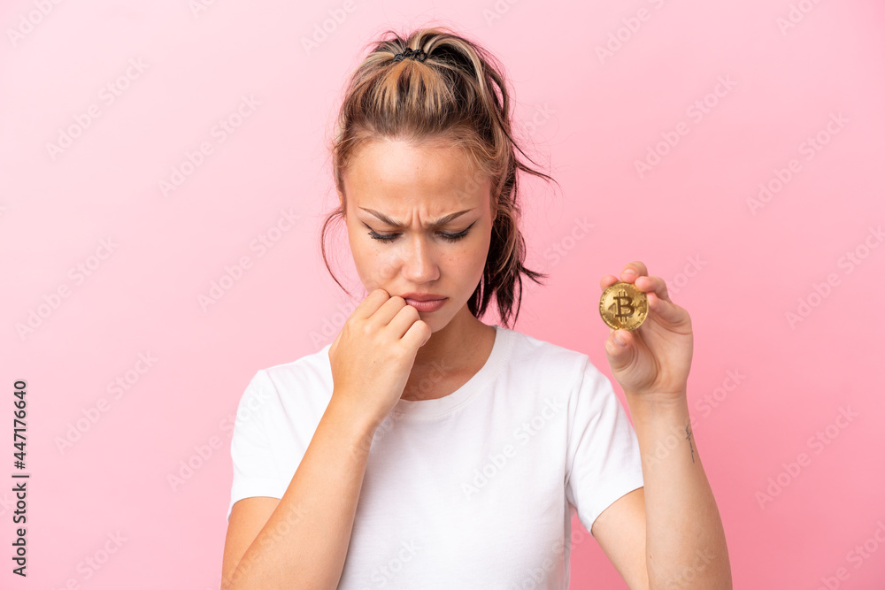 Teenager Russian girl holding a Bitcoin isolated on pink background having doubts