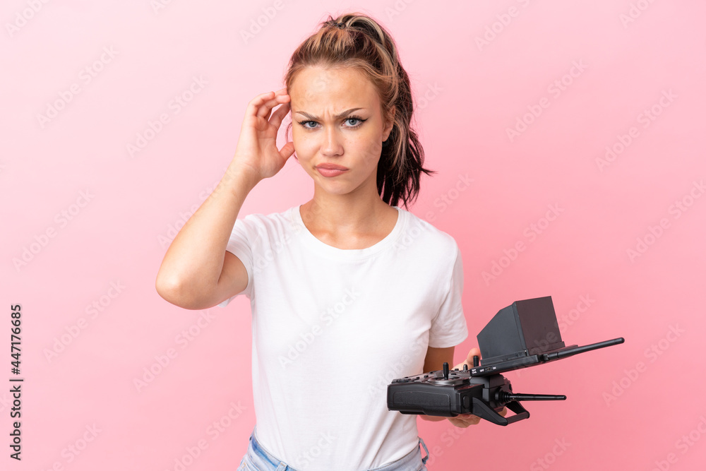 Teenager Russian girl holding a drone remote control isolated on pink background having doubts Teenager Russian girl holding a drone remote control isolated on pink background having doubts