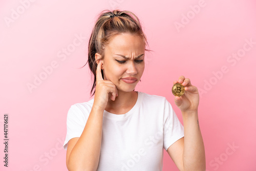 Teenager Russian girl holding a Bitcoin isolated on pink background frustrated and covering ears