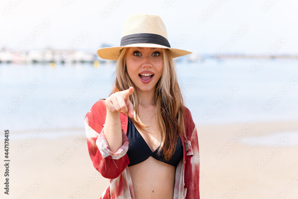 Young pretty woman in summer holidays at beach surprised and pointing front