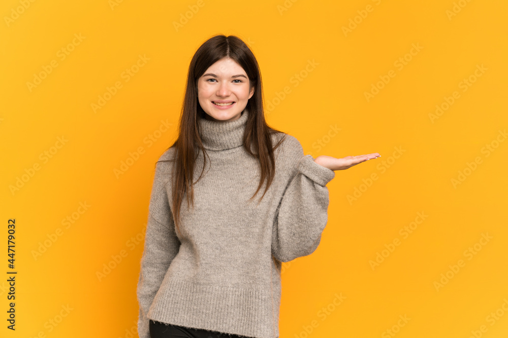 Young Ukrainian girl isolated on yellow background holding copyspace imaginary on the palm to insert an ad Young Ukrainian girl isolated on yellow background holding copyspace imaginary on the palm to insert an ad