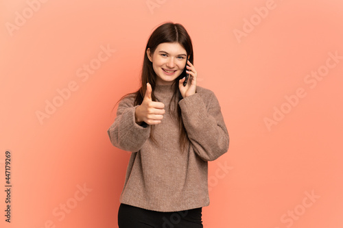 Young Ukrainian girl isolated on pink background keeping a conversation with the mobile while doing thumbs up