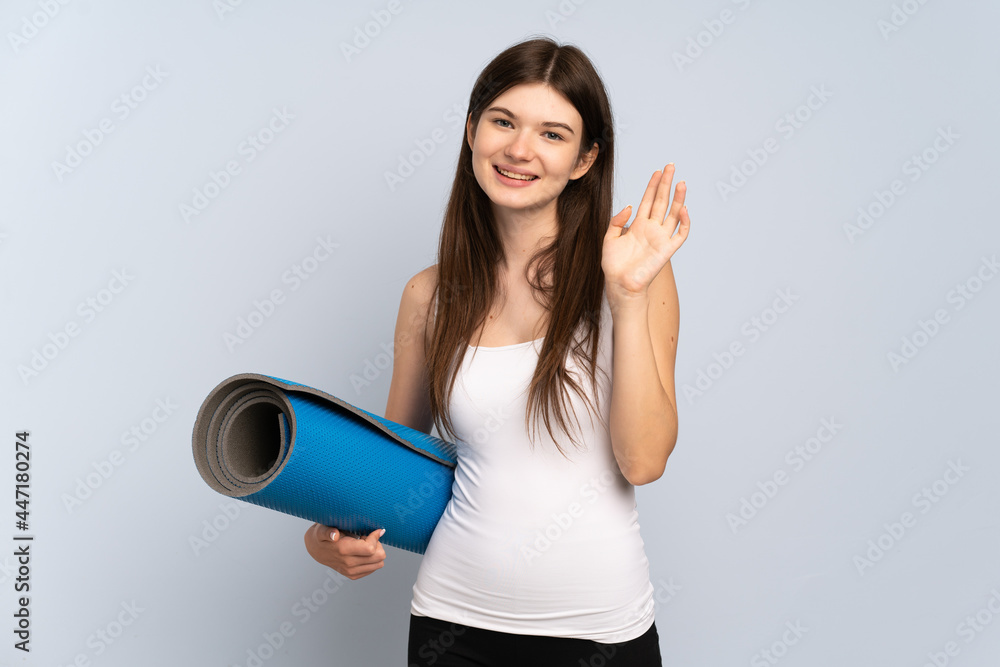 Young Ukrainian sport girl going to yoga classes while holding a mat saluting with hand with happy expression Young Ukrainian sport girl going to yoga classes while holding a mat saluting with hand with happy expression