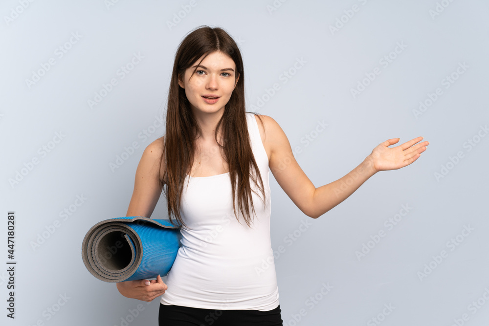 Young Ukrainian sport girl going to yoga classes while holding a mat extending hands to the side for inviting to come Young Ukrainian sport girl going to yoga classes while holding a mat extending hands to the side for inviting to come