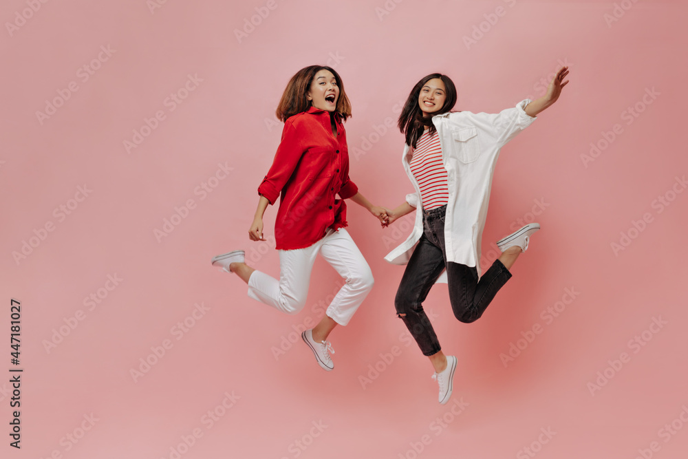 Happy women jump on isolated background. Tanned Asian girls in stylish outfits move on pink backdrop. Happy women jump on isolated background. Tanned Asian girls in stylish outfits move on pink backdrop.