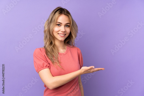 Teenager Russian girl isolated on purple background presenting an idea while looking smiling towards © luismolinero