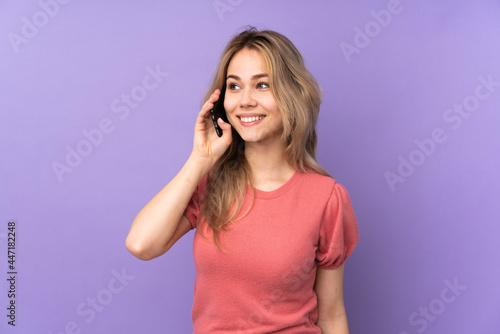 Teenager Russian girl isolated on purple background keeping a conversation with the mobile phone