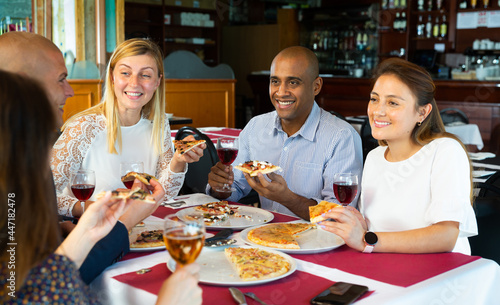 Cheerful multiracial group of friends having fun and enjoying dinner with delicious pizza in cozy italian restaurant