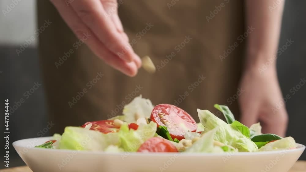 Woman's hand sprinkles pine nuts salad. Close-up . Woman's hand sprinkles pine nuts salad. Close-up .