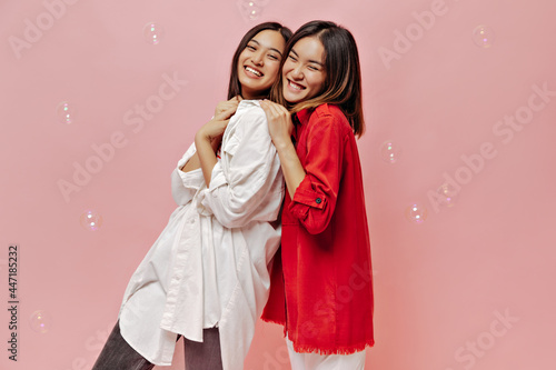 Cute short-haired girls in red and white shirts laugh on pink background with bubbles. Pretty women in good mood smile sincerely on isolated.