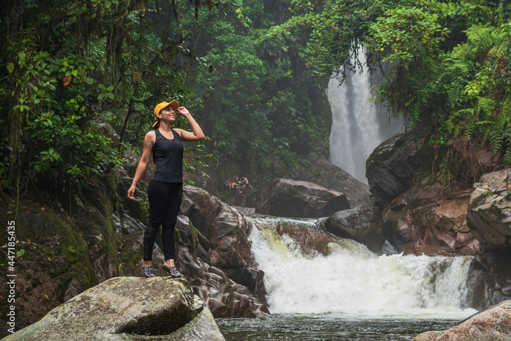 WOMAN STOPS ON A ROCK IN FRONT OF A WATERFALL