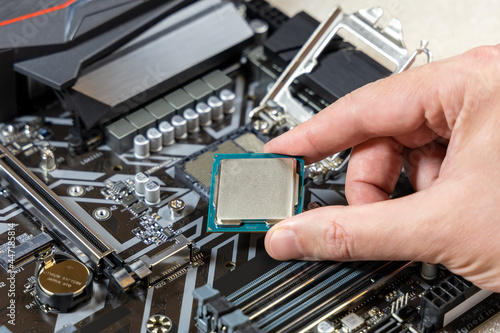 Installing the CPU into a socket on the motherboard. The technician holds the blank central processing unit of the PC against the background of the motherboard. PC assembly and upgrade concept
