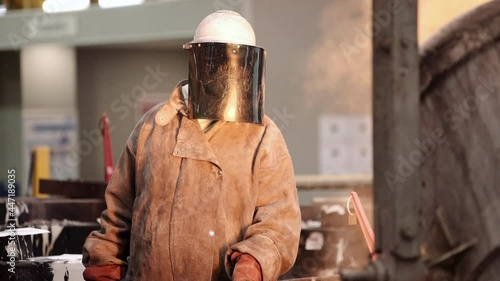 An industrial foundry worker in protective clothing supervising the careful ladle pouring of molten steel into the casting mold. photo