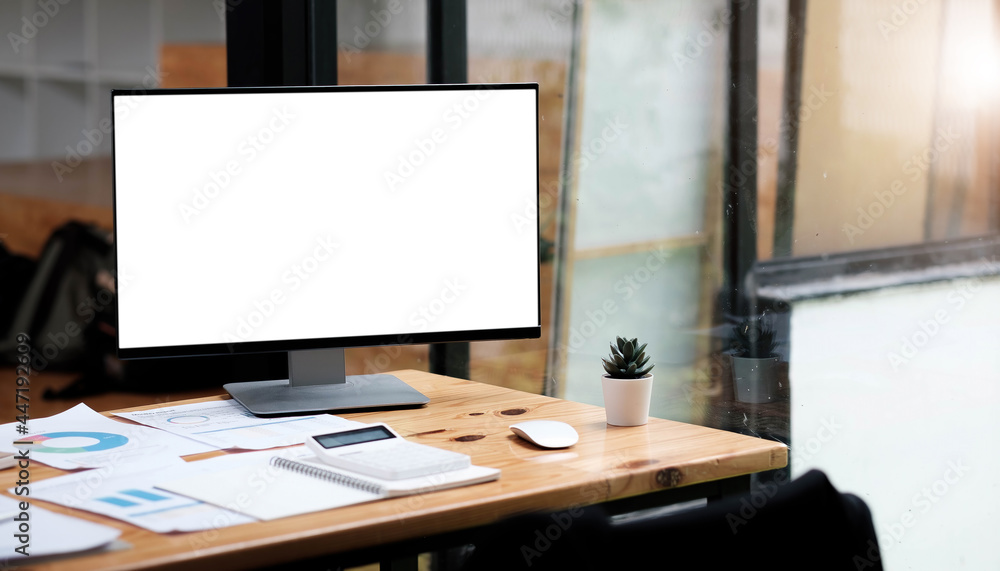 Computer laptop with white blank screen putting on wooden working desk that surrounded by coffee cup, stack of books, potted plant, pencils over comfortable living room windows as background. Computer laptop with white blank screen putting on wooden working desk that surrounded by coffee cup, stack of books, potted plant, pencils over comfortable living room windows as background.