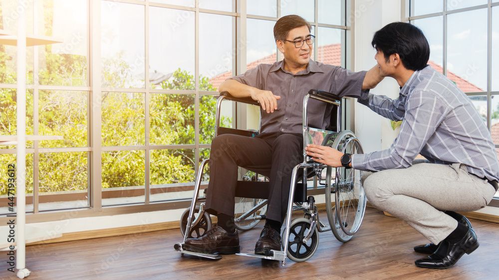 Asian senior disabled businessman in wheelchair discuss interacting together with the team in the office. The old man in a wheelchair and his young son talking to and comforting bound father